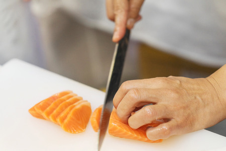 Hand of chef use knife preparing a fresh salmon on a cutting board, Japanese chef in restaurant slicing raw salmon, ingredient for seafood dishの写真素材