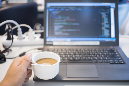 Fresh coffee for great ideas. office man working on laptop and holding cup of coffee while sitting at his working placeの写真素材