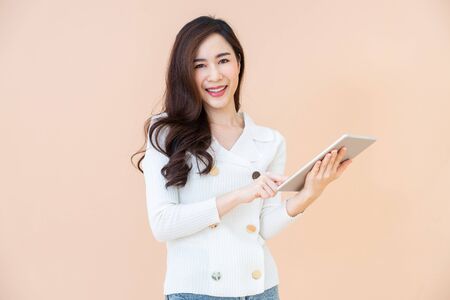 Portrait of Beautiful young smiling happy woman browsing internet on digital tablet computer isolated on a orange backgroundの写真素材