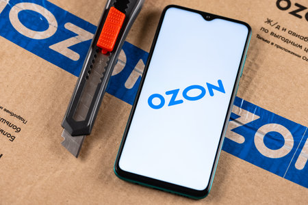 Ozon logo on the screen smartphone closeup. Ozon is one of the first e-commerce companies in Russia. Smartphone on the background of the parcel and box cutter.のeditorial素材