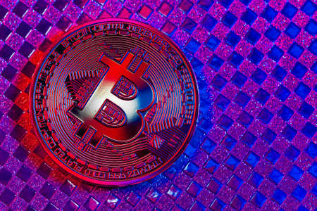 Golden bitcoin in a mixed blue and red light on a colorful backgroundの写真素材