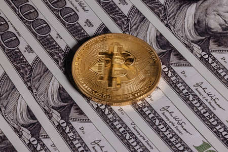 Gold bitcoin on one hundred dollar bills. The coin reflects the eyes of Benjamin Franklin.