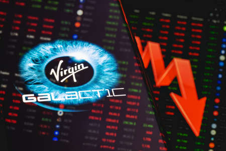 Kazan, Russia - May 31, 2021: Virgin Galactic is company developing commercial spacecraft. Virgin Galactic logo on the background of a large red arrow pointing down. Falling stock price.のeditorial素材