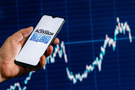 Kazan, Russia - August 7, 2021: Activision Blizzard, Inc. is an American video game holding company. A smartphone with the Activision Blizzard logo in a hand. Stock chart on the background.のeditorial素材