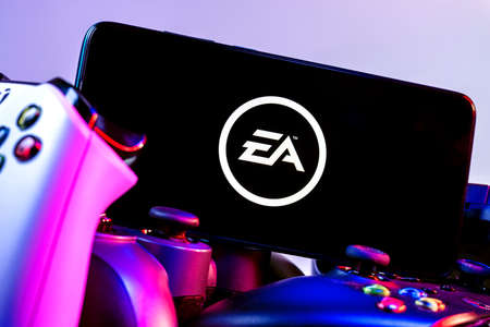 Kazan, Russia - August 14, 2021: Electronic Arts Inc. is an American video game company. A smartphone with the Electronic Arts logo on the screen on the pile of the gamepads.のeditorial素材
