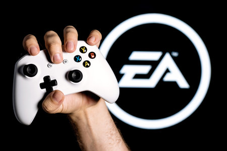 Kazan, Russia - August 14, 2021: Electronic Arts Inc. is an American video game company. A white gamepad clutched in the hand on the black background with the logo of Electronic Arts.のeditorial素材