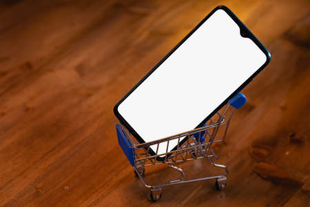 Mockup image of a smartphone with the blank white screen in shopping cart on a wooden table.の写真素材