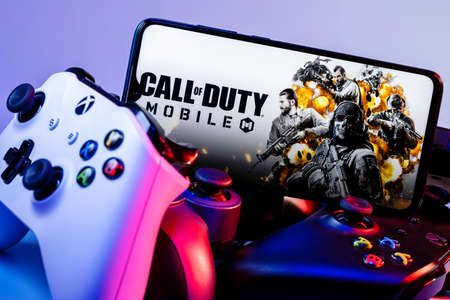 Kazan, Russia - September 07, 2021: Call of Duty: Mobile is a free-to-play shooter game. A smartphone with the frame from Call of Duty on the pile of the gamepads.のeditorial素材