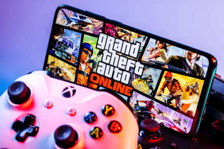 Kazan, Russia - September 17, 2021: Grand Theft Auto Online is an online multiplayer action-adventure game. A smartphone with the frame from GTA Online on the pile of the gamepads.のeditorial素材