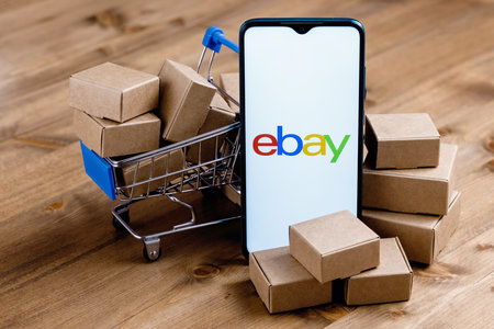 Kazan, Russia - Sep 25, 2021: eBay is an e-commerce corporation that offers online shopping, auction and marketplace services. Smartphone with eBay logo on the screen, shopping cart and parcels.のeditorial素材