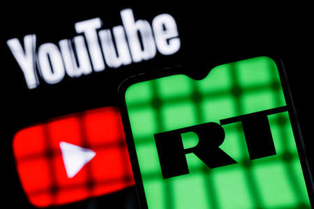 Kazan, Russia - Sep 29, 2021: Behind bars is a smartphone with the RT (Russia Today) logo on the background of the Youtube logo. Blocking RT (Russia Today) YouTube channels.のeditorial素材
