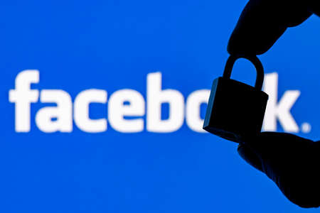 Kazan, Russia - Oct 19, 2021: Fingers hold a closed security lock on the background of the facebook...