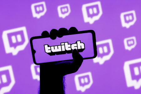 Kazan, Russia - Oct 28, 2021: Smartphone with the Twitch live streaming service logo on the screen in a clenched hand on the background of Twitch logosのeditorial素材