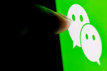 Kazan, Russia - Nov 16, 2021: The finger reaches for the WeChat messenger logo on the smartphone...