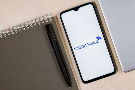 Kazan, Russia - Dec 13, 2021: Smartphone with Credit Suisse bank logo on wooden table next to laptop and business plannerのeditorial素材