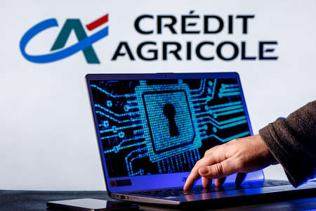 Kazan, Russia - Dec 16, 2021: Laptop with lock symbol on screen on background of Credit Agricole bank logo. Finger points to lock symbol. Concept of data hacking.のeditorial素材