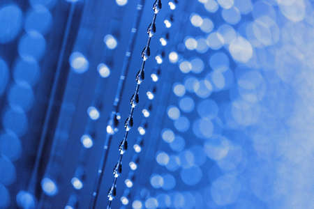 Close-up of a lot of water droplets flowing down the threads in blue light. Shallow depth of field.の写真素材