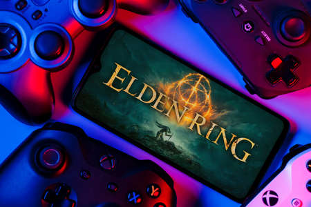 Kazan, Russia - Feb 22, 2022: Elden Ring is an action role-playing video game. Smartphone with frame from Elden Ring on screen surrounded by gamepads.のeditorial素材