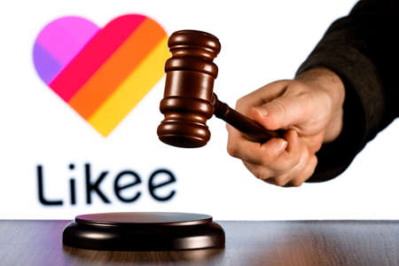 Kazan, Russia - Mar 01, 2022: Gavel in judge hand against background of Likee short video sharing service logo. The concept of trial.のeditorial素材