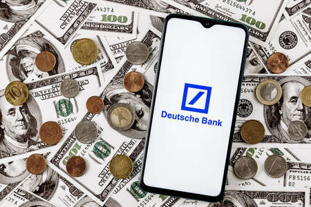 Kazan, Russia - Apr 04, 2022: Smartphone with Deutsche bank logo surrounded by variety of metal coins on background of dollar billsのeditorial素材