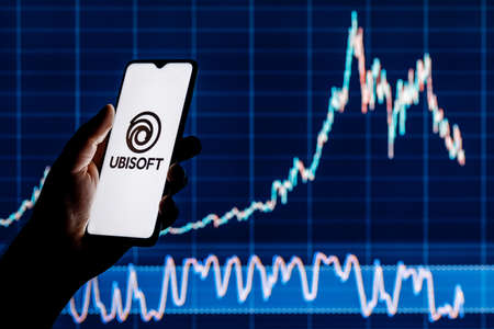 Kazan, Russia - Apr 15, 2022: Ubisoft is French video game company. Smartphone with Ubisoft logo in hand. Stock chart on background.のeditorial素材