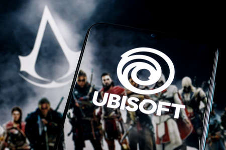 Kazan, Russia - Apr 15, 2022: Ubisoft is French video game company. Ubisoft logo on smartphone screen. Frame from Assassin Creed franchise game on background.のeditorial素材