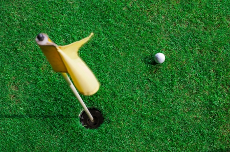 A golf ball and a hole with yellow flag の写真素材
