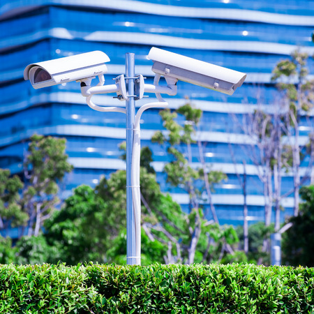 CCTV camera or surveillance operaiting with blue building and park in backgroundの写真素材