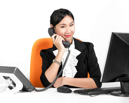 Young pretty business woman using phone with desktop computerの写真素材