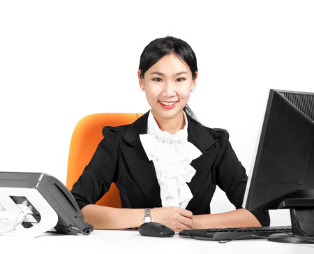 Young pretty business woman sitting on desk with desktop computer and phoneの写真素材