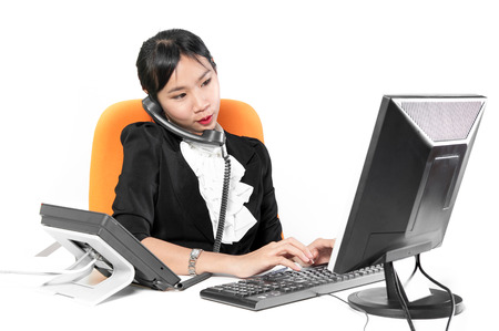 Young pretty business woman using phone with desktop computerの写真素材