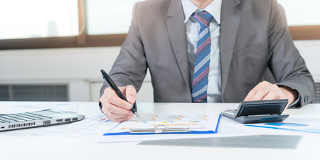 Businessman analyzing report on chart with laptop and calculatorの写真素材
