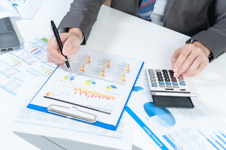 Businessman analyzing report on chart with laptop and calculatorの写真素材