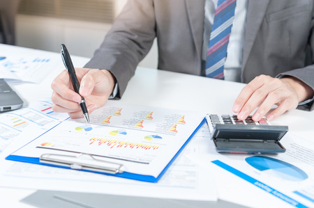Businessman analyzing report on chart with laptop and calculatorの写真素材