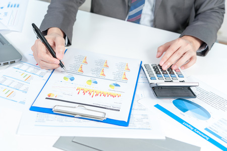 Businessman analyzing report on chart with laptop and calculatorの写真素材