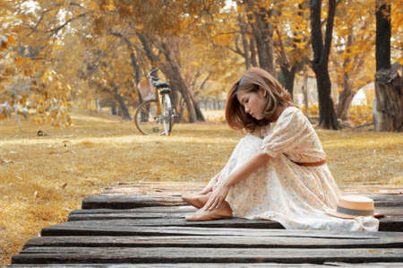beautiful young woman sit on wooden bridge in parkの写真素材