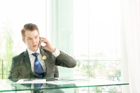 Handsome businessman in suit speaking on the phone in officeの写真素材