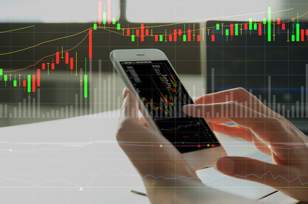 woman's hand using smart phone with digital layer of financial graph