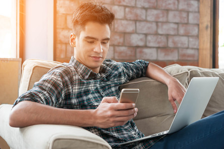 Businessman using smartphone and laptop writing on sofa in coffee shopの写真素材