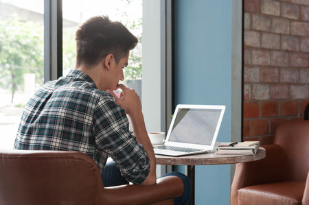 Businessman using laptop with tablet and pen on wooden table in coffee shop with a cup of coffeeの写真素材