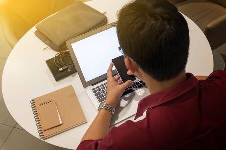 cropped shot of a young man working from home using smart phone and laptop computer, man at his workplace using technologyの写真素材