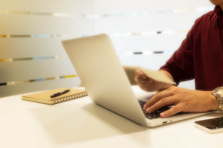 cropped shot of a young man using laptop computer with a piece of paper, man at his workplace using technologyの写真素材