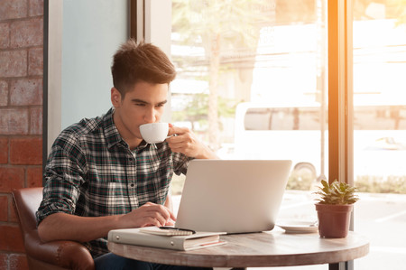 Businessman using laptop with tablet and pen on wooden table in coffee shop with a cup of coffeeの写真素材