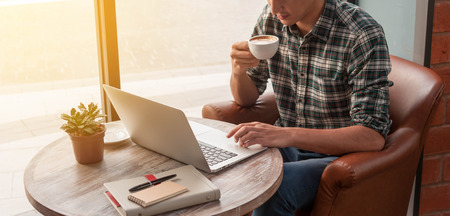Businessman using laptop with tablet and pen on wooden table in coffee shop with a cup of coffeeの写真素材