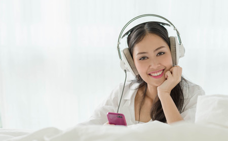 Beautiful teenage girl using smartphone with earphone at homeの写真素材