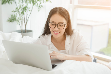 Woman Using Laptop In Bedroom by the window sit on floorの写真素材