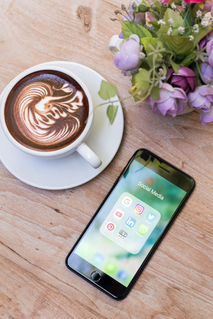CHIANG MAI, THAILAND - NOVEMBER 14th, 2016: Iphone7 Plus with icons of social media on screen with a cup of latte art on wooden tableのeditorial素材