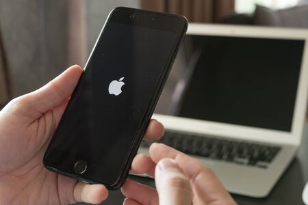 BANGKOK, THAILAND - NOVEMBER 26, 2016: Man using Iphone7 Plus jet black serie on opening screen of Apple inc. icon with macbook airのeditorial素材