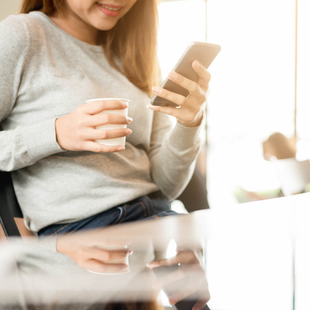 Woman using smartphone in coffee shop with image reflection on glass, internet of things conceptualのeditorial素材