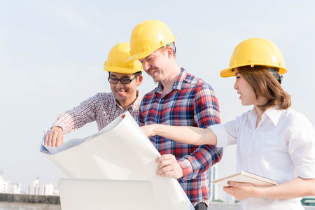 three construction engineers working outdoors in construction site with blueprintの写真素材